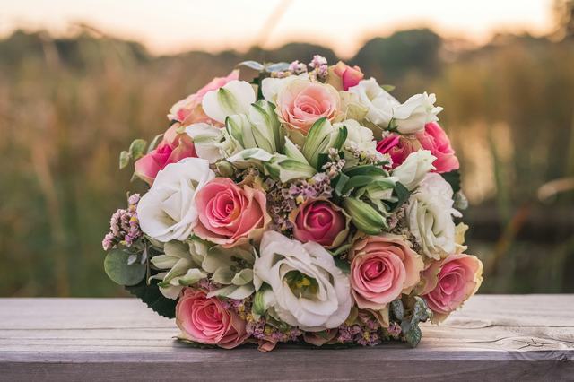 Een rond boeket met roze en witte rozen en lisianthus op een houten bank in de avondzon