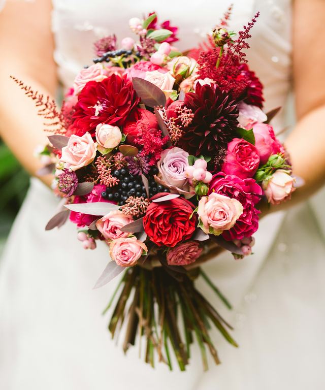 Een bruid met een bruidsboeket van rode en roze rozen en dahlia’s