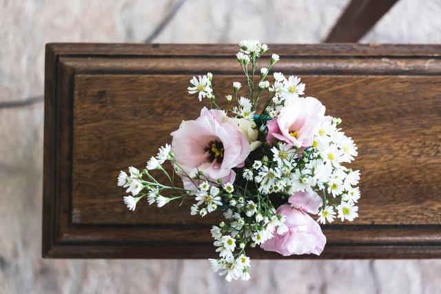 Een klein boeket met roze lisianthus en witte bloemetjes op een houten kist