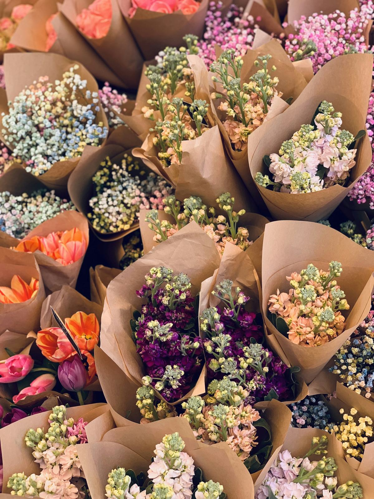 Boeketjes in bruin papier, dicht tegen elkaar: violier, tulpen en gipskruid