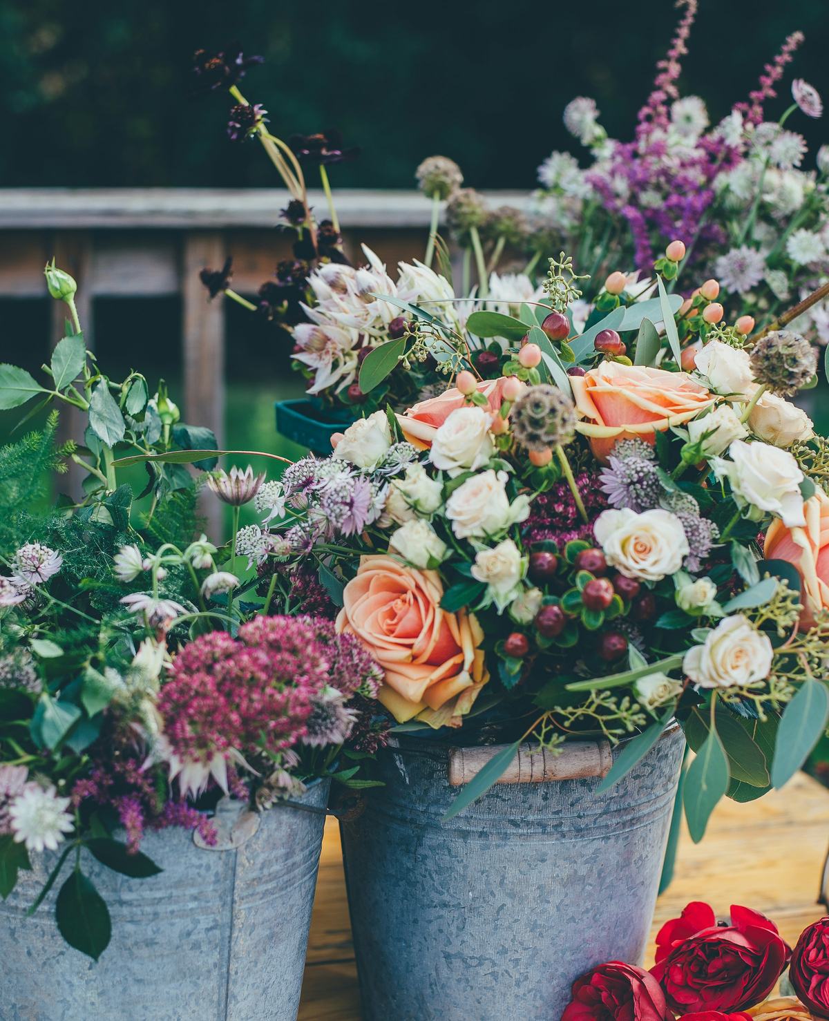 Zinken emmers vol rozen, astrantia en sedum op een houten tafel, met rode rozen ervoor